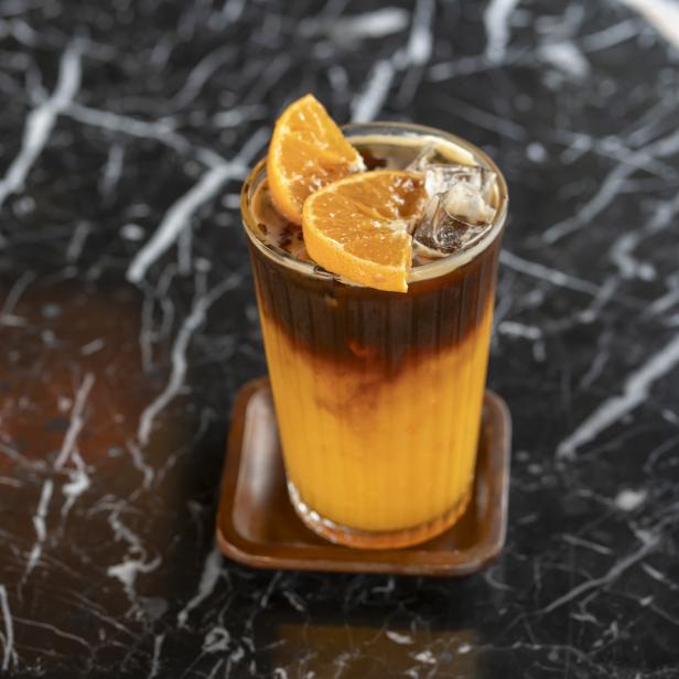 Ein Glas Eiskaffee mit Orangenscheiben auf einem Marmortisch.