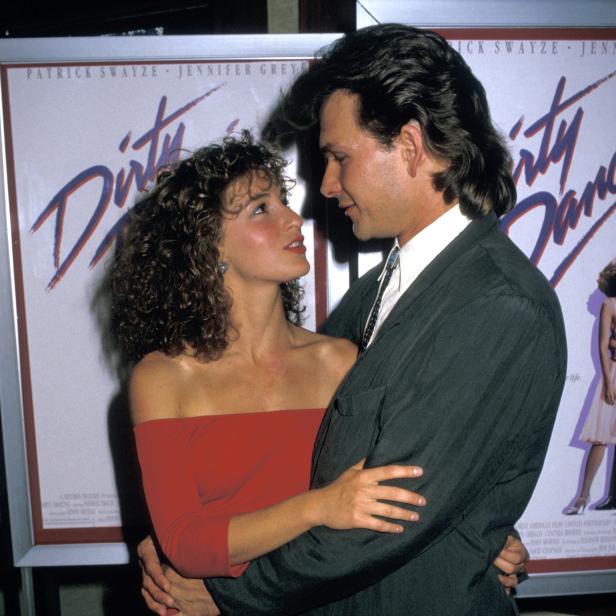 Patrick Swayze und Jennifer Grey umarmen sich vor einem Filmplakat von „Dirty Dancing“.