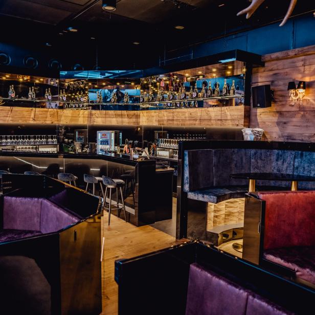 Innenansicht einer Bar mit dunklen Möbeln und einer Wand mit Holzverkleidung.