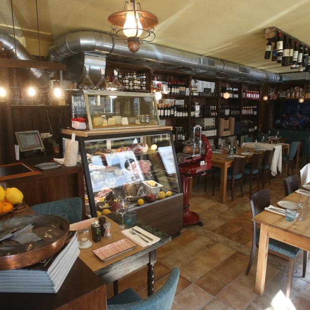 Innenansicht eines Restaurants mit Tischen, Stühlen und einer Theke mit Speisen.