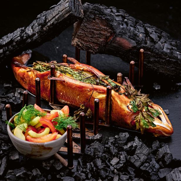 Ein geräucherter Fisch, gefüllt mit Kräutern, wird mit einem Salat serviert.