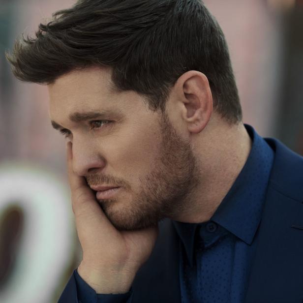 Michael Bublé in einem blauen Anzug, den Kopf in die Hand gestützt.