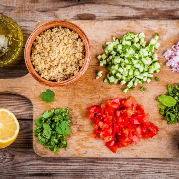 Zutaten für einen Quinoa-Salat auf einem Holzbrett angerichtet.