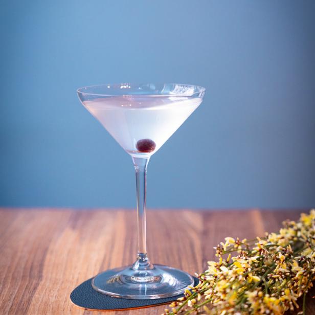 Ein Martini mit einer Kirsche in einem eleganten Glas auf einem Holztisch.