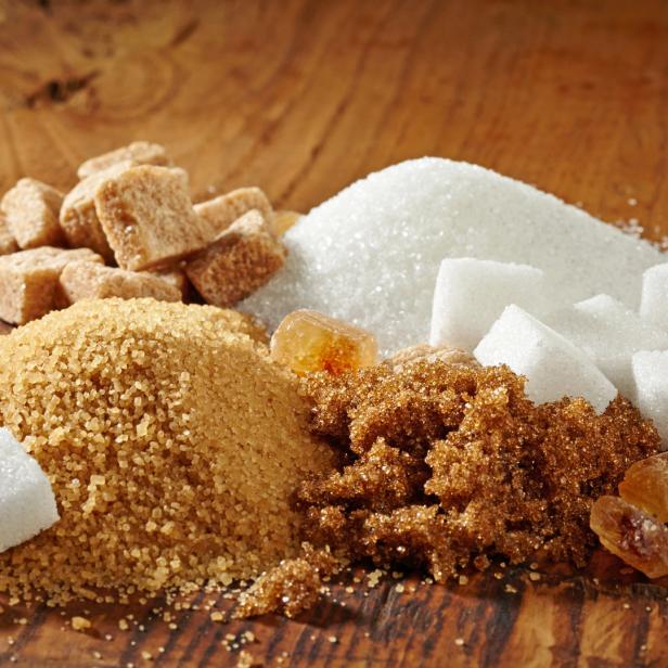 Verschiedene Zuckerarten, darunter weißer, brauner und Kandiszucker, auf einem Holztisch.