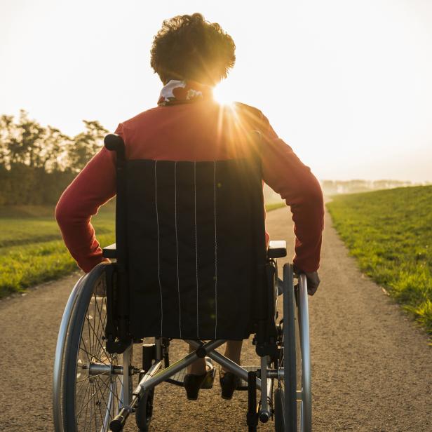 Eine Person im Rollstuhl fährt auf einem Weg in Richtung Sonnenuntergang.