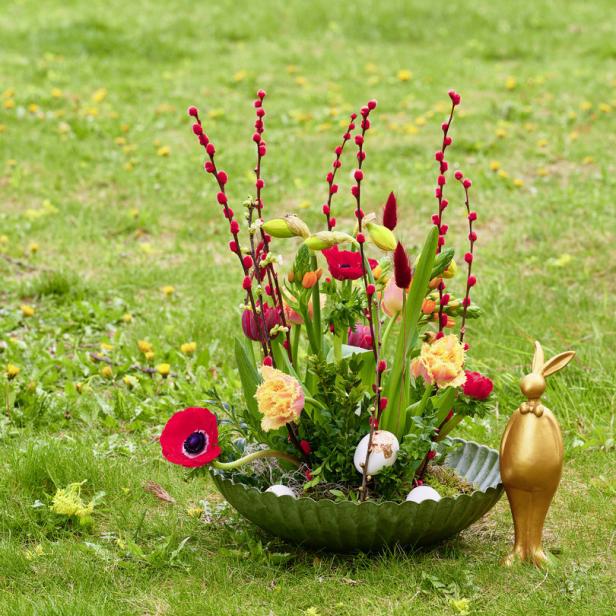 Ein österliches Blumenarrangement mit einem goldenen Hasen auf einer grünen Wiese.