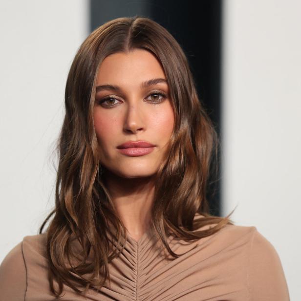 Porträt von Hailey Bieber mit braunem, gewelltem Haar und einem beigen Oberteil.