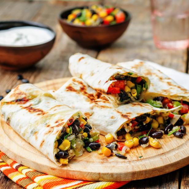Mehrere Burritos mit Bohnen, Mais und Paprika auf einem Holzbrett.