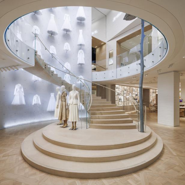 Innenansicht eines Bekleidungsgeschäfts mit einer Treppe und ausgestellten Kleidern.