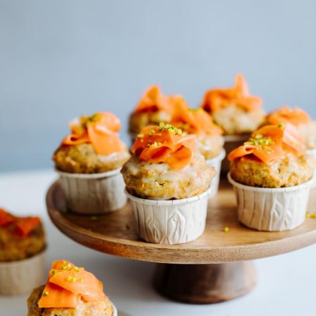 Mehrere Karottenmuffins mit Zuckerguss und gehackten Pistazien auf einem Holzständer.
