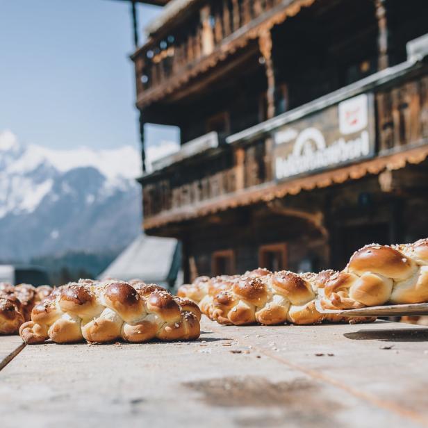 Geflochtene Zöpfe, vermutlich Brioche, werden vor einer Bergkulisse präsentiert.