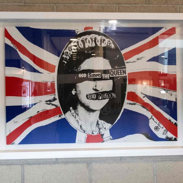 Ein gerahmtes Kunstwerk mit dem Motiv „God Save the Queen“ der Sex Pistols vor einer Union-Jack-Flagge.