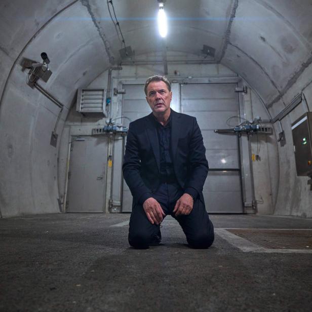 Ein Mann in Anzug kniet in einem unterirdischen Bunker.