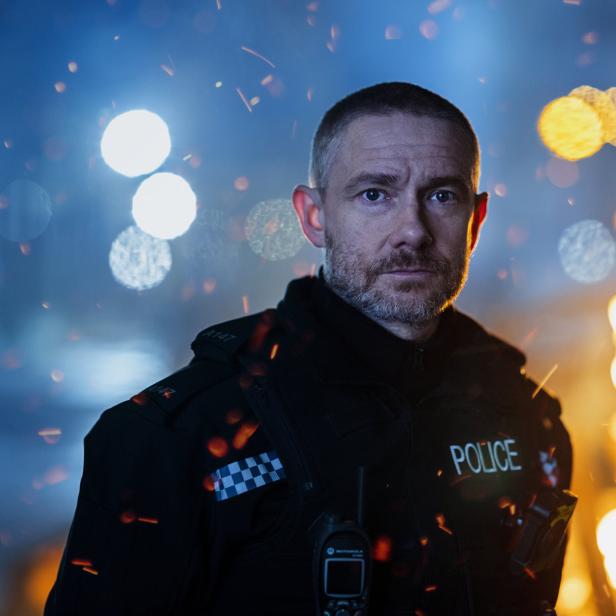 Ein Polizist steht vor einem Hintergrund aus Lichtern und Flammen.