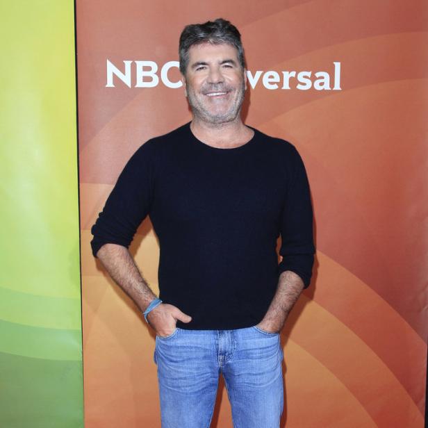 Simon Cowell posiert auf einem roten Teppich vor einem NBC-Universal-Logo.