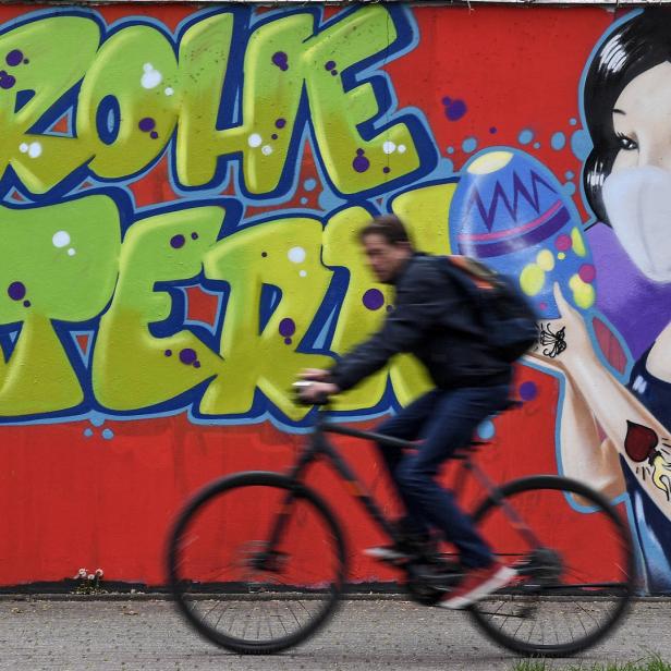 Ein Radfahrer fährt an einem Graffiti vorbei, das „Frohe Ostern“ und Schneewittchen mit Maske zeigt.