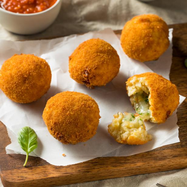 Mehrere goldbraune Arancini liegen auf einem Holzbrett mit Tomatensauce.