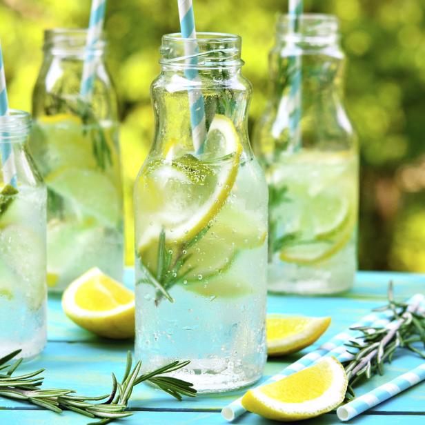 Limonade mit Zitrone und Rosmarin in Glasflaschen mit blau-weiß gestreiften Strohhalmen.