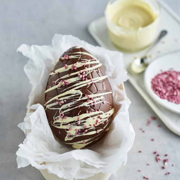 Ein schokoladiges Osterei mit weißer Glasur und rosa Streuseln in einer kleinen Schale.