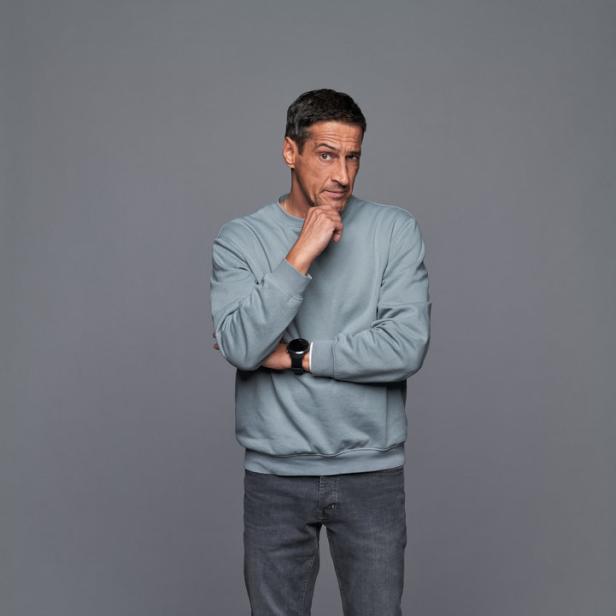 Ein Mann in Jeans, Pullover und Turnschuhen steht nachdenklich da.
