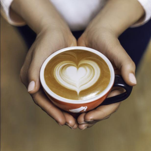 Eine Person hält eine rote Tasse mit einem Latte Art Herz.