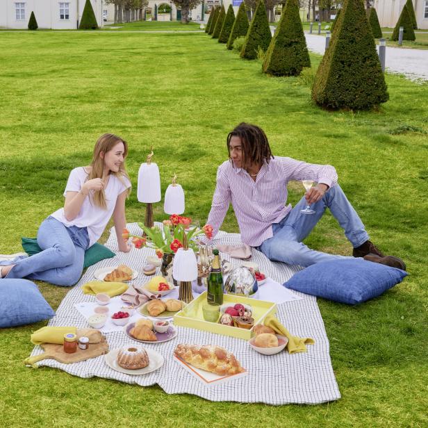Ein Paar genießt ein Picknick mit Gebäck und Getränken auf einer Wiese.