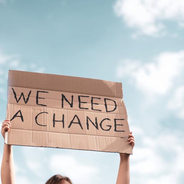 Eine Person hält ein Schild mit der Aufschrift „We need a change“ in den Himmel.