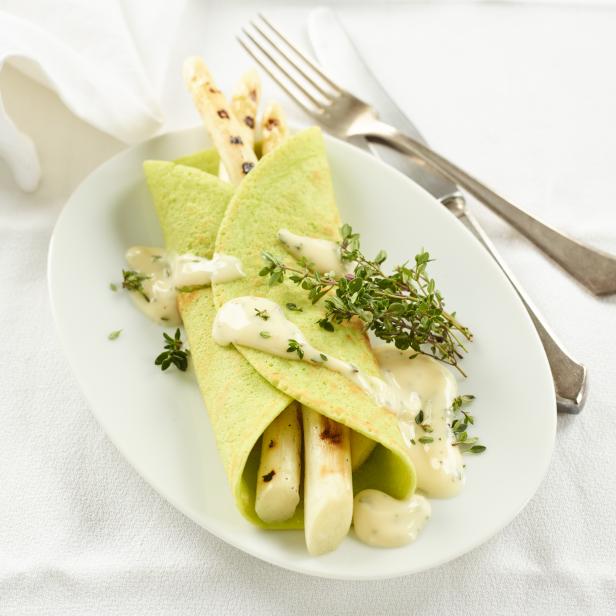 Grüne Crêpes gefüllt mit Spargel und Sauce auf einem Teller angerichtet.