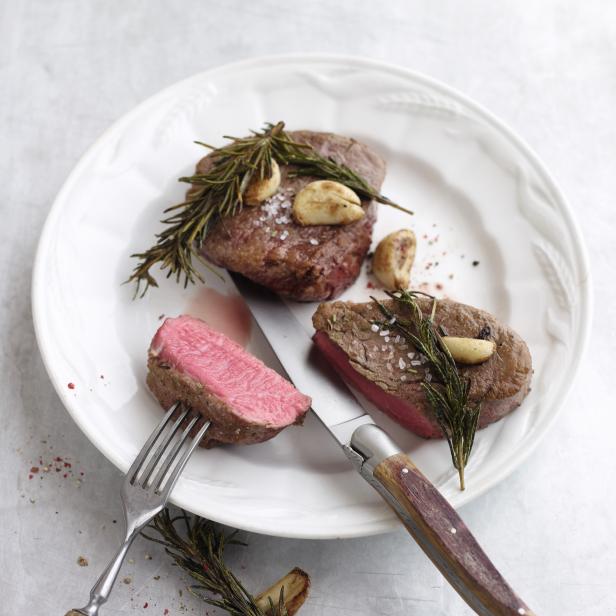 Zwei rosa gebratene Steaks mit Rosmarin und Knoblauch auf einem Teller.