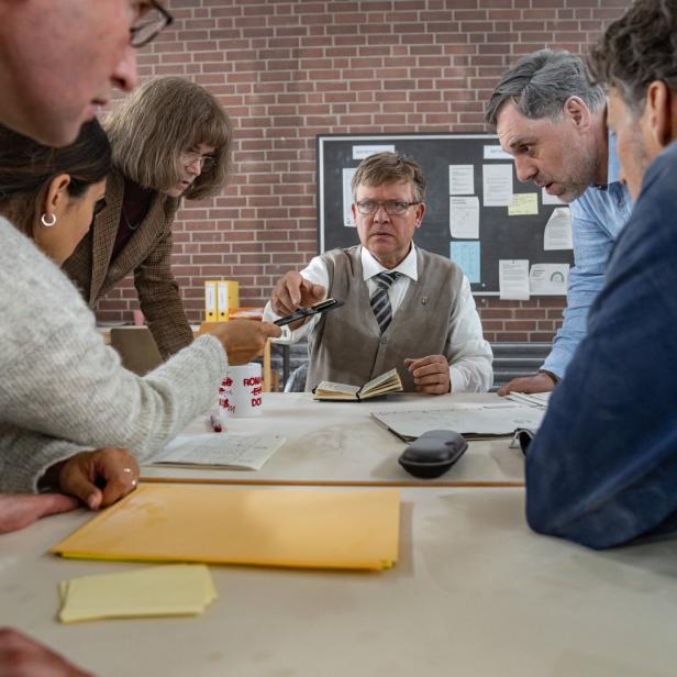 Eine Gruppe von Menschen steht um einen Tisch und diskutiert über Dokumente.