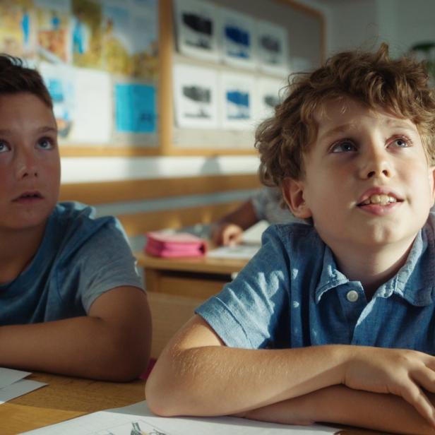 Zwei Jungen sitzen in einem Klassenzimmer und schauen nach oben.