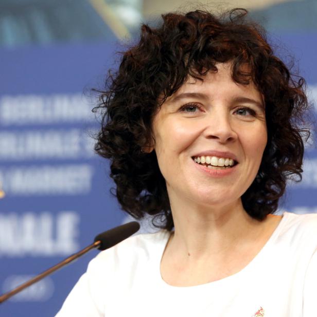 Eine lächelnde Frau mit lockigem Haar vor einem Hintergrund der Berlinale.