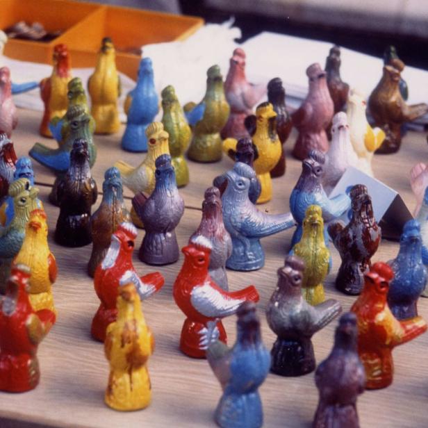 Viele bunte Taubenfiguren stehen auf einem Tisch zum Verkauf.