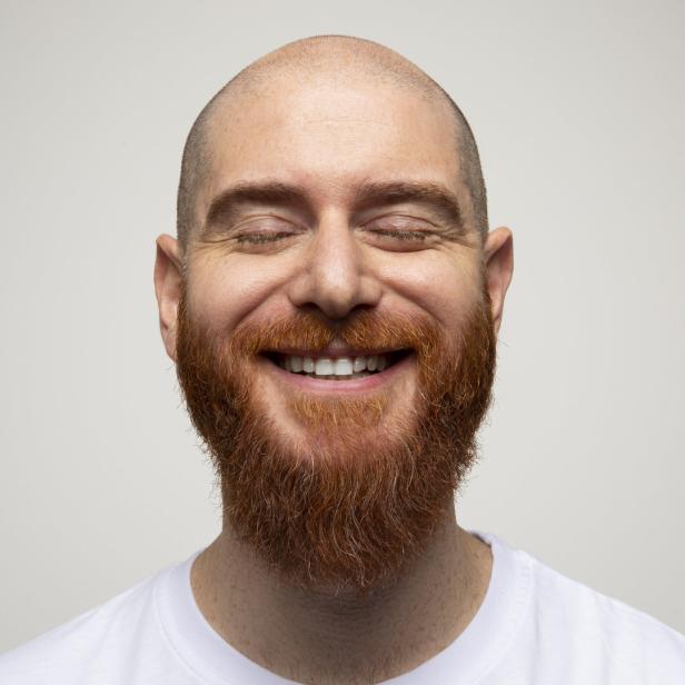 Ein lachender, glatzköpfiger Mann mit rotem Bart und geschlossenen Augen.
