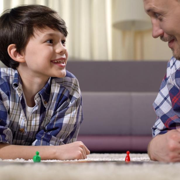 Ein Vater und sein Sohn spielen ein Brettspiel auf dem Teppich.