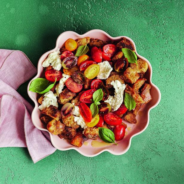 Ein Panzanella-Salat mit Tomaten, Brot, Mozzarella und Basilikum wird in einer rosa Schüssel serviert.