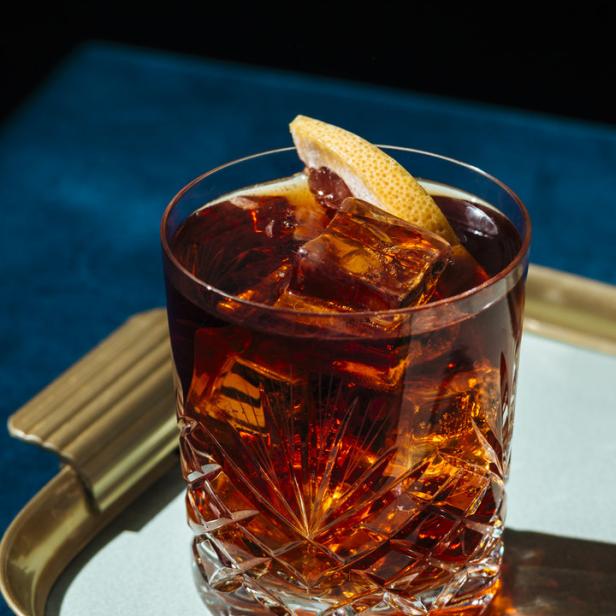 Ein Cocktail mit Eiswürfeln und einer Grapefruitzeste in einem Kristallglas.