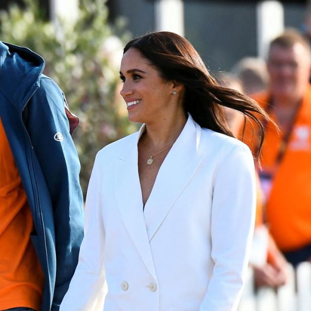 Meghan Markle in einem weißen Hosenanzug lächelt in die Ferne.