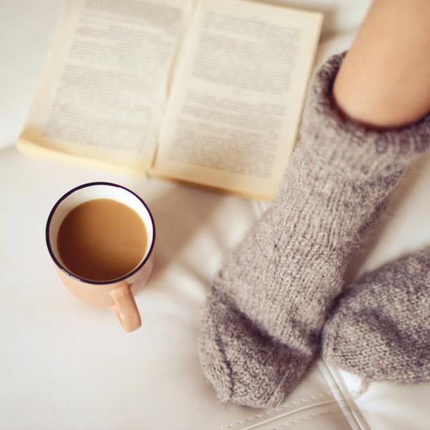 Ein Paar Wollsocken, eine Tasse Kaffee und ein offenes Buch auf einem Sofa.