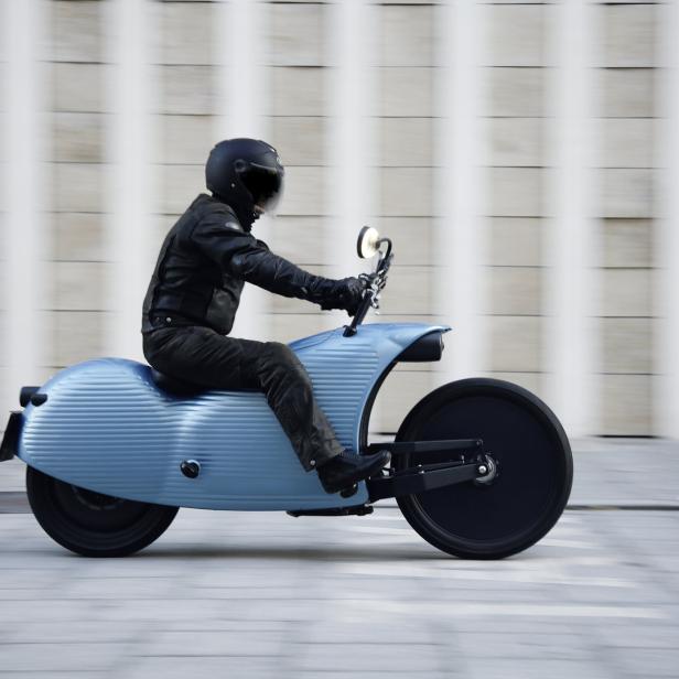 Ein Fahrer auf einem blauen Johammer J1 Motorrad vor einer Wand.