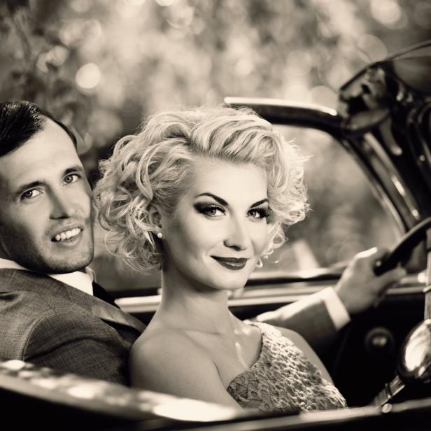 Ein Paar im Oldtimer-Cabriolet, die Frau am Steuer.