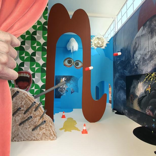 Eine surreale Kunstinstallation mit verschiedenen Objekten und Malereien in einem Raum.