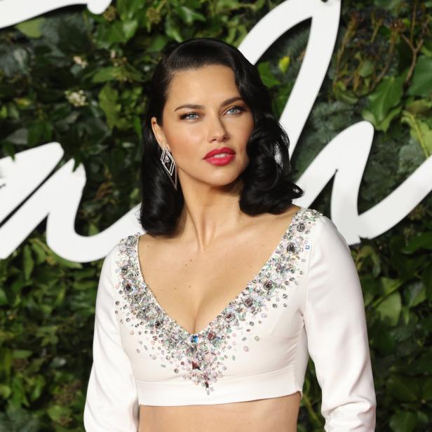 Adriana Lima trägt ein weißes, bauchfreies Oberteil mit Schmucksteinen.