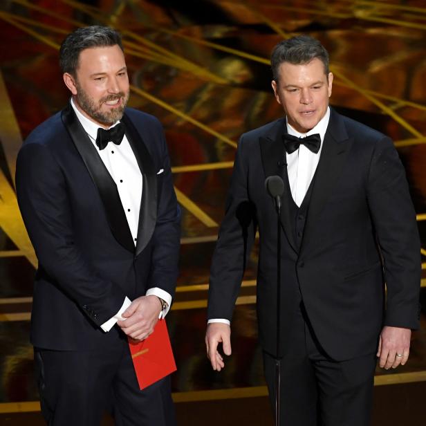 Ben Affleck und Matt Damon in Anzügen auf einer Bühne.
