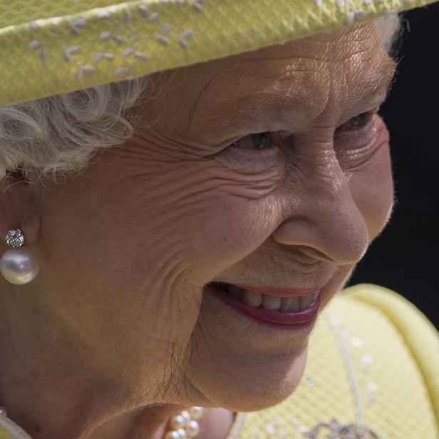 Nahaufnahme von Königin Elizabeth II. mit gelbem Hut und Perlenohrringen.