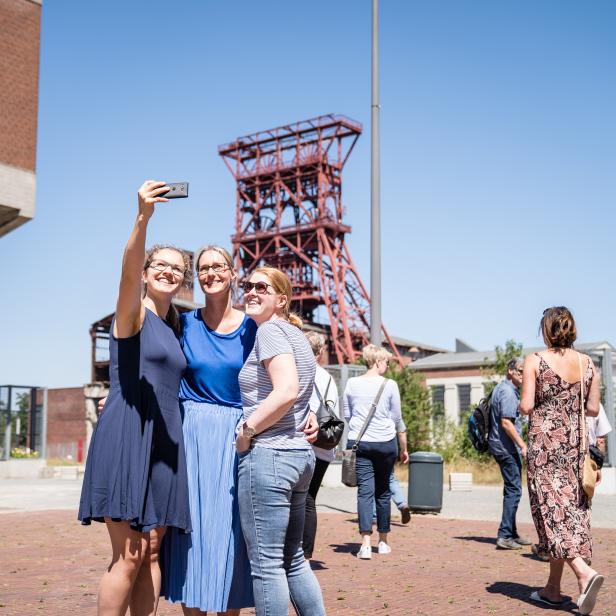 Drei Frauen machen ein Selfie vor einem Förderturm auf dem Gelände Zollverein in Essen.