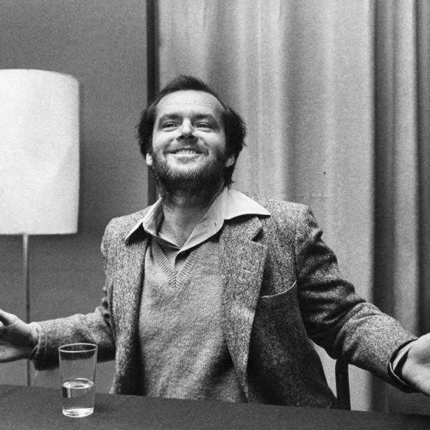 Jack Nicholson sitzt an einem Tisch und lächelt in die Kamera.
