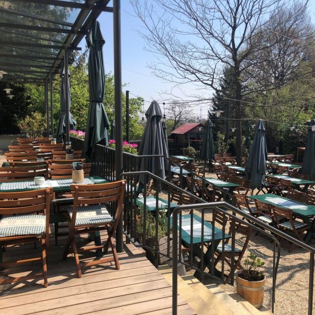 Ein Biergarten mit Tischen und Stühlen unter Sonnenschirmen an einem sonnigen Tag.