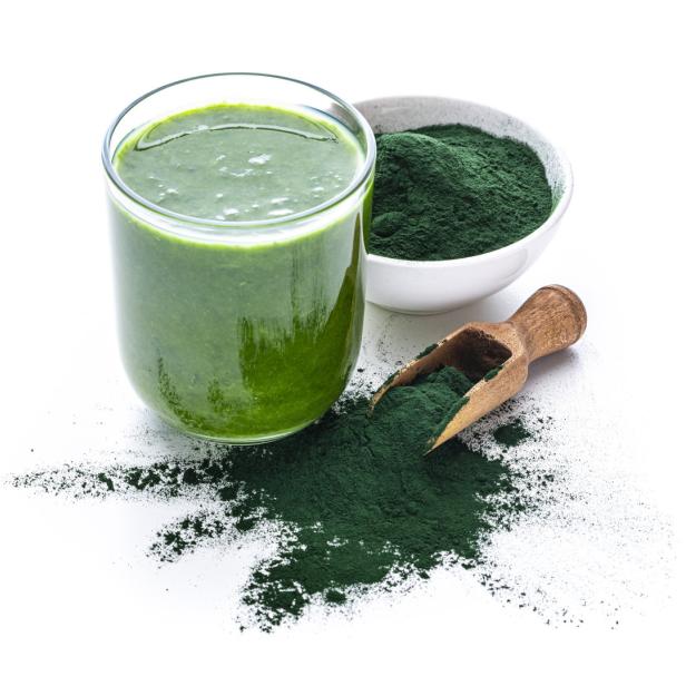 Ein Glas grüner Smoothie mit Spirulinapulver und einem Messlöffel.